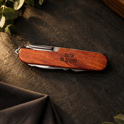 Personalized groomsmen pocket knife with a rosewood handle, engraved JUSTIN and the wedding date, closed on dark slate beside a folded charcoal pocket square
